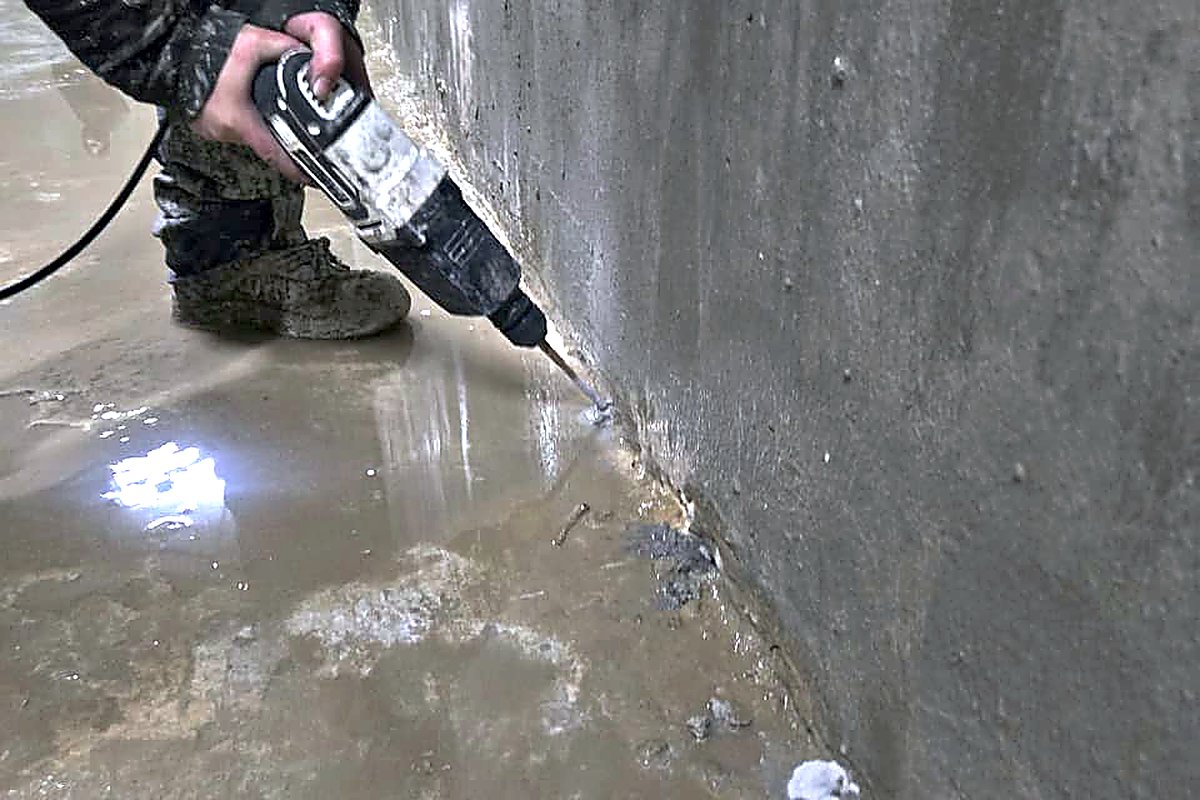 Operario perforando la base de un muro de hormigón con rotomartillo para instalar un puerto de inyección